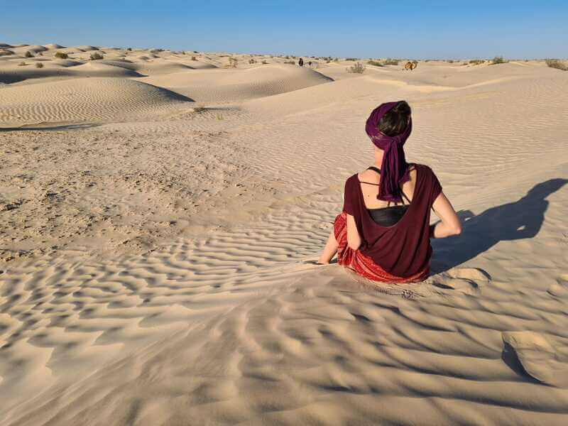 Claire de dos face aux dunes du désert et au ciel bleu, dans un moment d’introspection et de contemplation